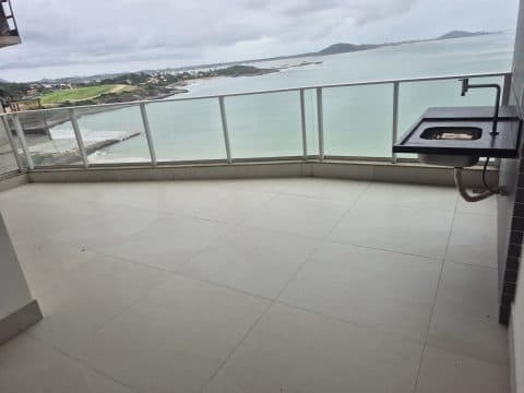 Varanda ampla com piso claro, guarda-corpo de vidro e pia em granito com vista para o mar.