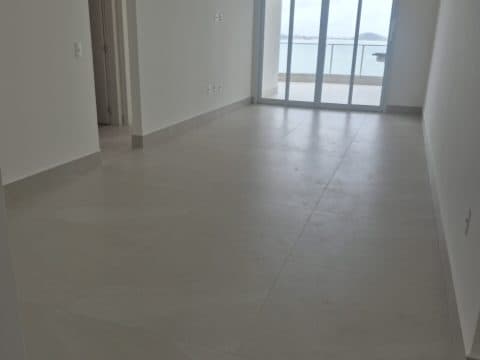 Sala interna com piso claro em porcelanato, paredes brancas e acesso à varanda com porta de vidro.