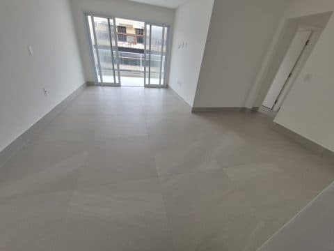 Sala ampla com piso em tons claros e acesso para a varanda.
