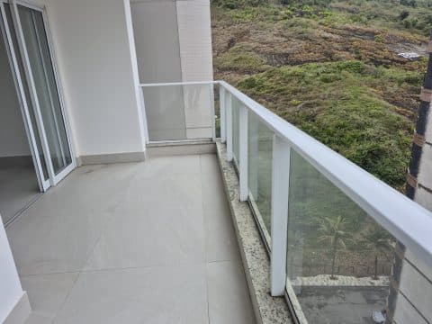 Varanda ampla com piso claro, guarda-corpo de vidro e vista para área verde