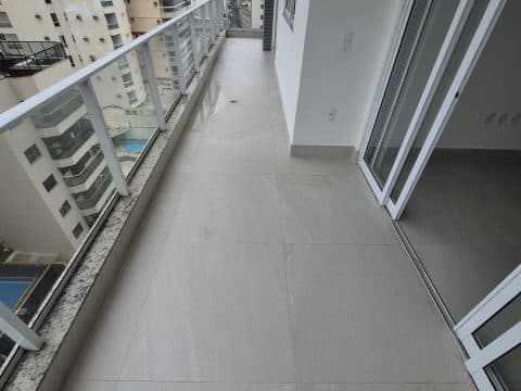 Varanda comprida com piso claro, guarda-corpo de vidro e acesso por porta de vidro