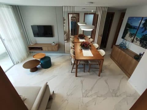 Vista ampla da sala de estar e jantar com painel de TV, mesa de jantar e detalhes em painel ripado.