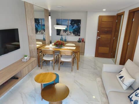 Sala de estar e jantar decorada com mesa de madeira, cadeiras estofadas, sofá e porta de entrada em madeira.