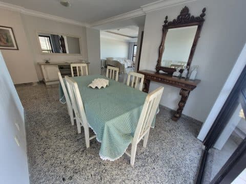 Sala de jantar com mesa coberta, cadeiras brancas e espelho decorativo na parede.